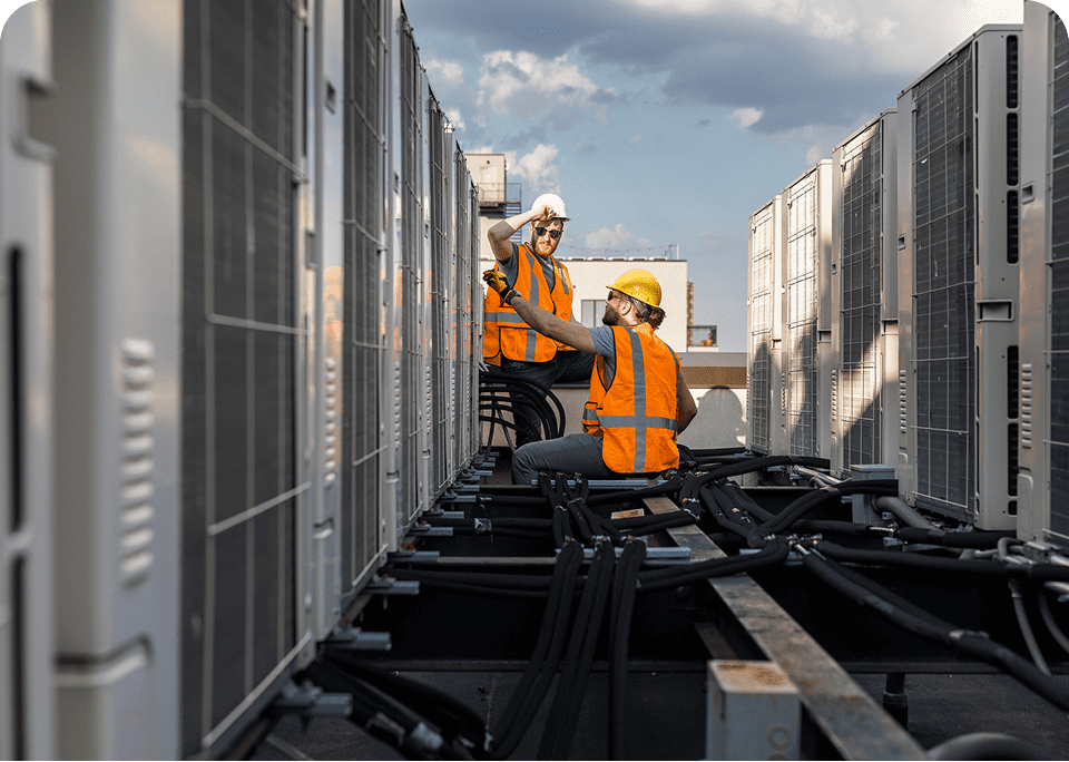 Workers inspecting rooftop HVAC units, cloudy sky.