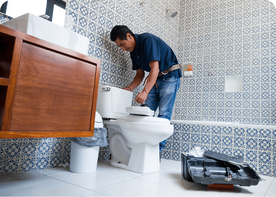 Person fixing toilet in tiled bathroom.